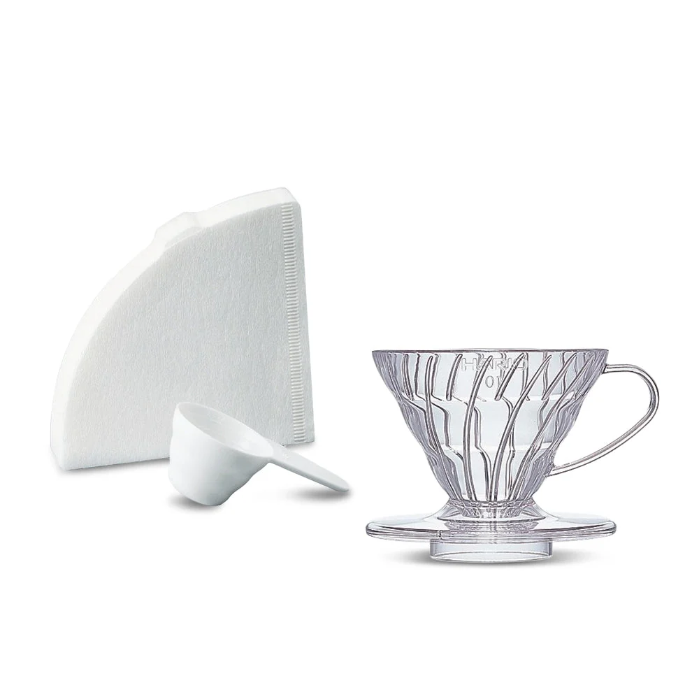 Clear plastic Hario V60 dripper beside paper filters and a white measuring scoop